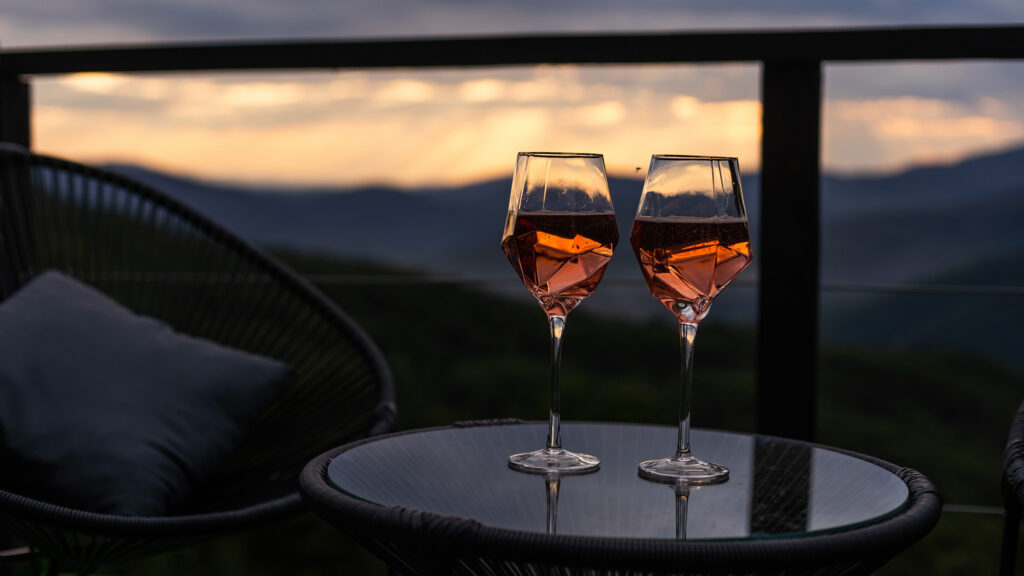 Zwei Gläser mit Rosewein stehen auf einem kleinen Tisch auf einem Balkon mit einem schönen Sonnenuntergang im Hintergrund