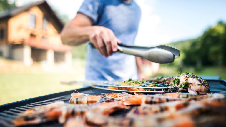 Ein Mann ohne Blähungen grillt Meeresfrüchte auf BBQ an einem sonnigen sommerigen zTag im Hinterhof.