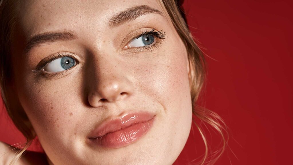 Junge Frau blickt achtsam zur Seite, Nahaufnahme ihres Gesichts vor rotem Hintergrund – Symbol für Selbstwahrnehmung, Hormonbalance und emotionale Veränderungen in den Phasen des weiblichen Zyklus.