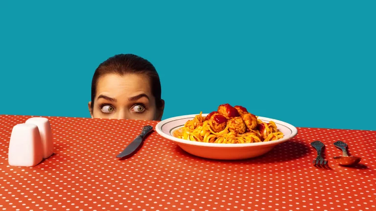 Eine Frau blickt auf ein Teller am Tisch - sie hat ein schlechtes Gewissen, es zu essen. Sie praktiziert intermittierendes Fasten.